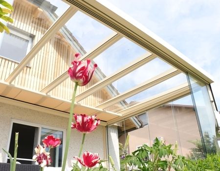 Ein Sommergarten in weiß mit Unterglas-Markise und Blumen im Vordergrund