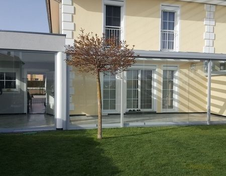 Eine Terrasse mit einem Glasdach und Glasschiebetüren bei einem gelben Haus