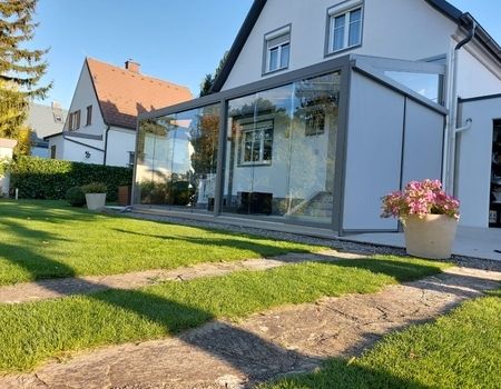 Ein großer Sommergarten mit Glasschiebetüren  auf einer großen Terrasse. Es befinden sich auch Senkrechtmarkise auf der Seite