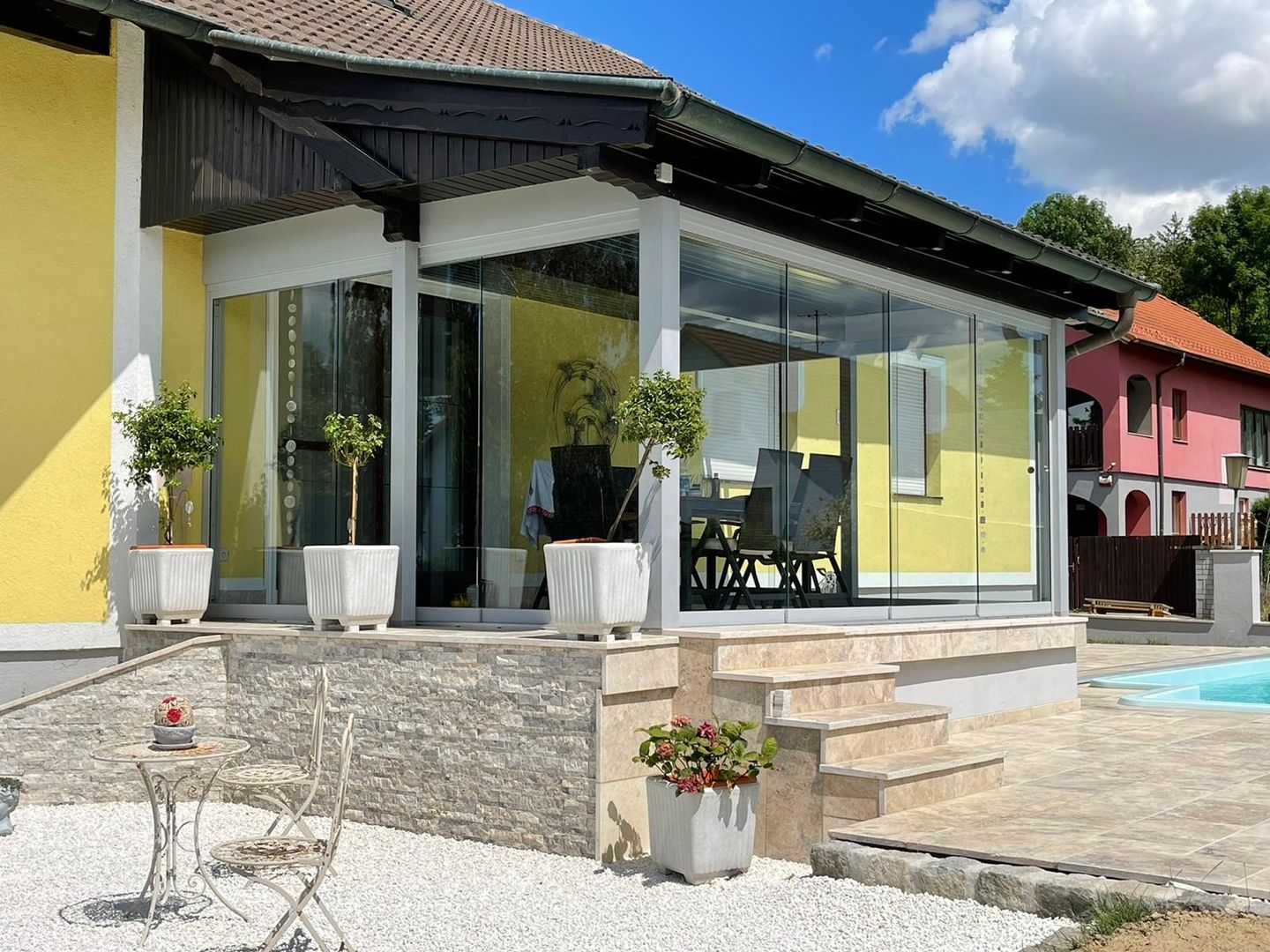 Ein Sommergarten mit Glanzglas Schiebesystem auf einer schönen Terrasse mit hellen Fliesen