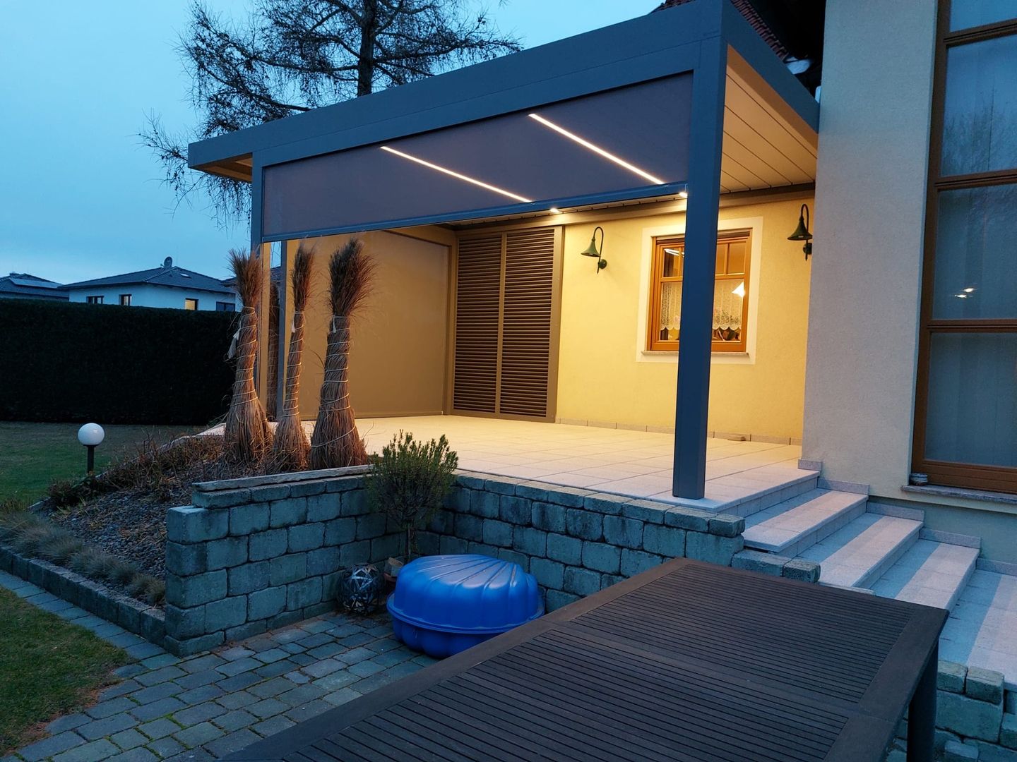 Eine Lamellenüberdachung mit schiebbaren Lamellen und Senkrechtmarkisen und LED-Beleuchtung