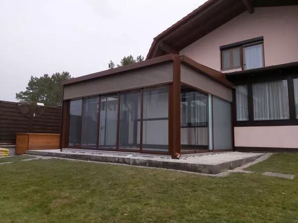 Ein brauner Sommergarten mit Glasschiebetüren und Senkrechtmarkisen vorne und auf der Seite