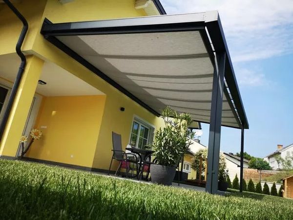 Ein gelbes Gebäude mit einer Terrassenüberdachung mit Unterglas-Markise